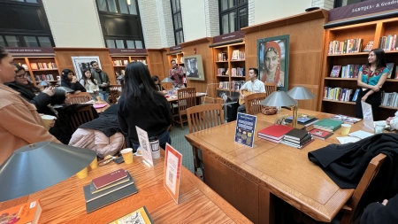 People gathering around in a library to listen to a student play guitar. 