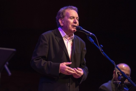 Manolis Mitsias stands on stage with a microphone