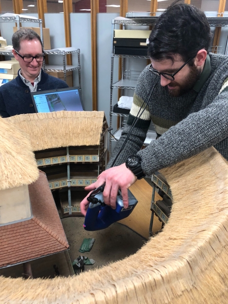 A man holds a scanner near a model of the Globe Theater