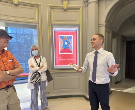 A man standing in lobby with poster behind him talks to two library users