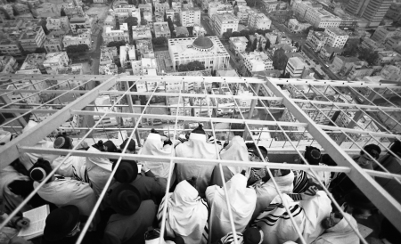 A group of men wearing prayer shawls and phylacteries stand on a skyscraper overlooking Tel Aviv.