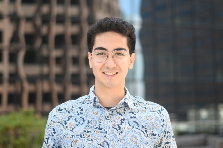 Simon Levien, wearing glasses and a bright, floral shirt, smiles at the camera