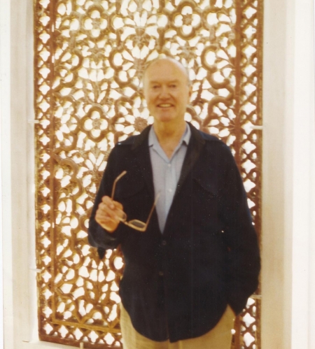 Stuart Cary Welch stands, holding his glasses, and smiles at the camera