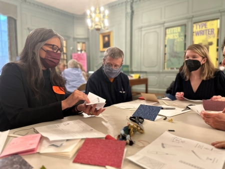 Three people at a table holding paper and pamphlet-making tools.