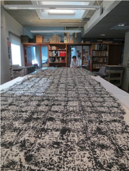 A long, cloth print extends across a table to a person sitting in the distance