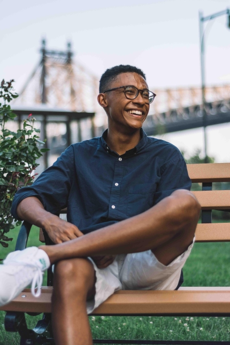 William Lohier, wearing glasses, shorts and a collared shirt, sits on a bench in front of the Golden Gate Bridge and smiles