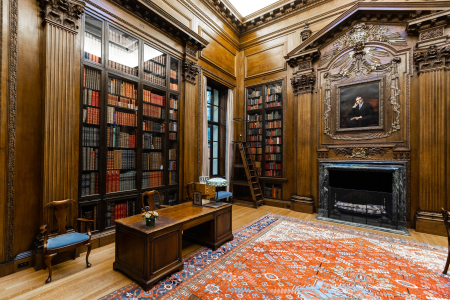 The Harry Elkins Widener memorial room in Widener - with wood panels, a desk, and a portrait of Widener.