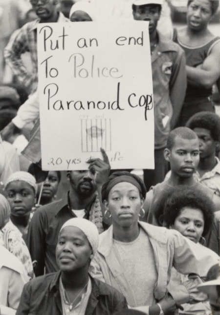 Crowd of Black Americans with one man holding a sign against "paranoid police"