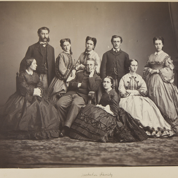 Salted paper print showing nine members of the Hecksher Family: two parents and seven adult children.  The father is seated in the center with his right hand tucked into his jacket, left arm resting on the arm of the chair and left hand gently raising to his chin. His wife is seated to his left looking at him. Standing behind them and facing front are, from left to right, a bearded son, two daughters, another son, and a daughter. Two other daughters are seated in front, one kneeling by the father. 