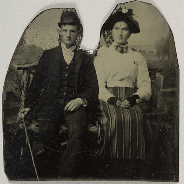Black and white tintype photo of a couple (white man and woman) sitting side by side, with a space in between cut out leaving jagged outlines