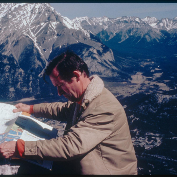 A picture of a man reading a map with mountains in the background. 