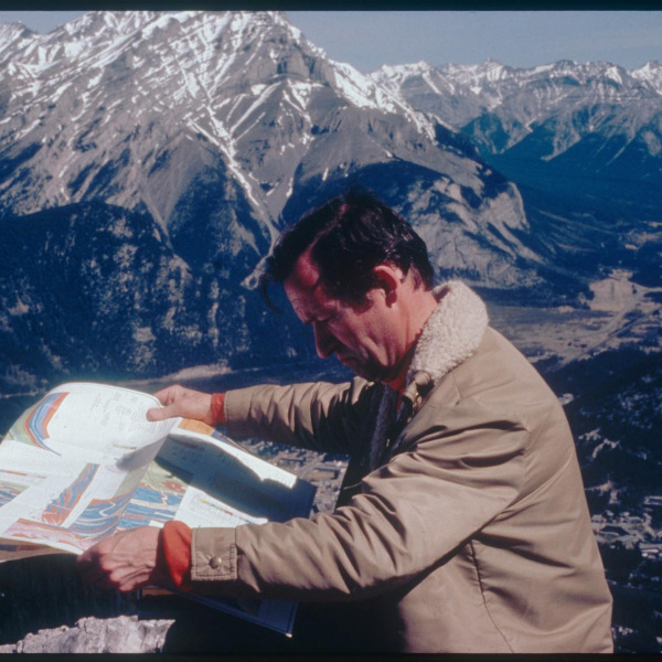 A picture of a man reading a map with mountains in the background. 