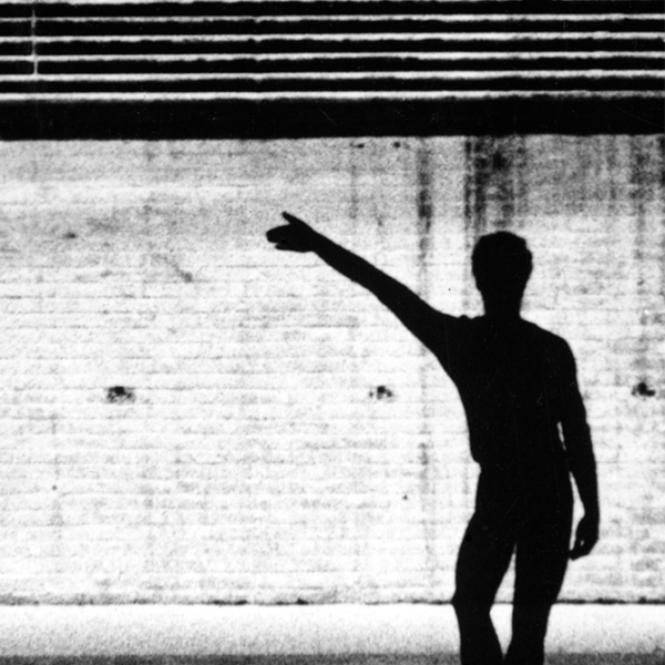 Dancer Merce Cunningham in silhouette, standing with right arm extended and right knee slightly bent.