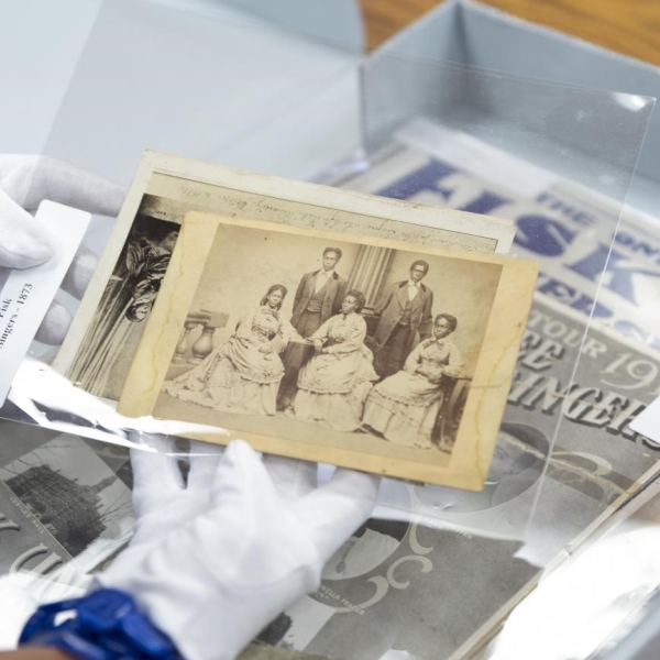 hands with gloves on handling old photographs in an exhibit