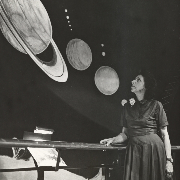 A Woman stands in front of an astronomy exhibition, looking up at a model of Saturn and other planets.