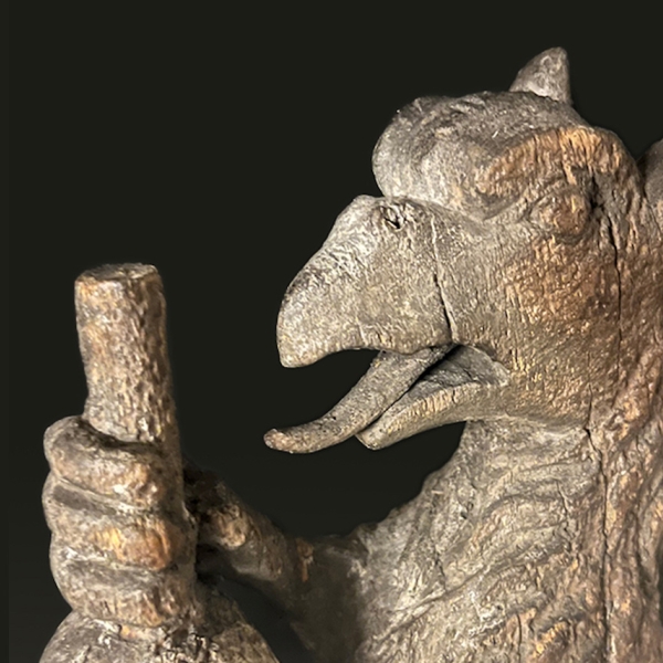 Wood carving of a griffin with its mouth open and claws clutching the stem of an ink ball.