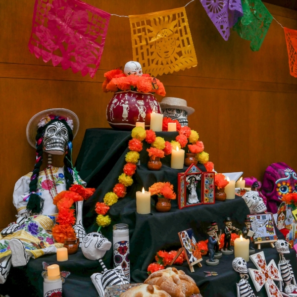 Traditional Day of the Dead alter decorated with folk-craft skeletons, flower garlands, paper cutouts, and candles. 