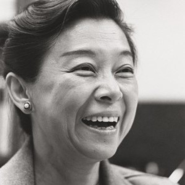 A headshot of a woman wearing a blazer, with her hair pulled up. She is smiling widely.