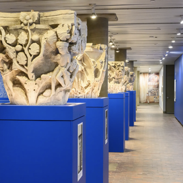 Image of the exhibition featuring a line of intricately carved column capitals displayed on blue pedestals