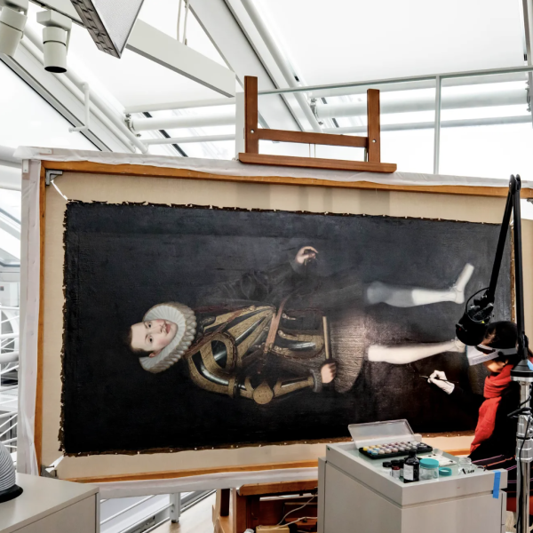 Photograph of a conservationist working on a large oil portrait