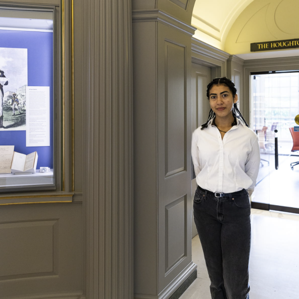 Photo of the author wearing a white dress shirt and black slacks standing in the atrium of Houghton library next to a display case