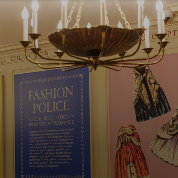 An image of the Fashion Police exhibit with its wall text through a doorway