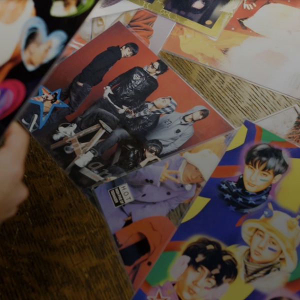 An image of a person examining a display a k-pop fandom collection items at a table. There's a lot of colorful posters and items on the table, and a pair of hands are holding up a poster.
