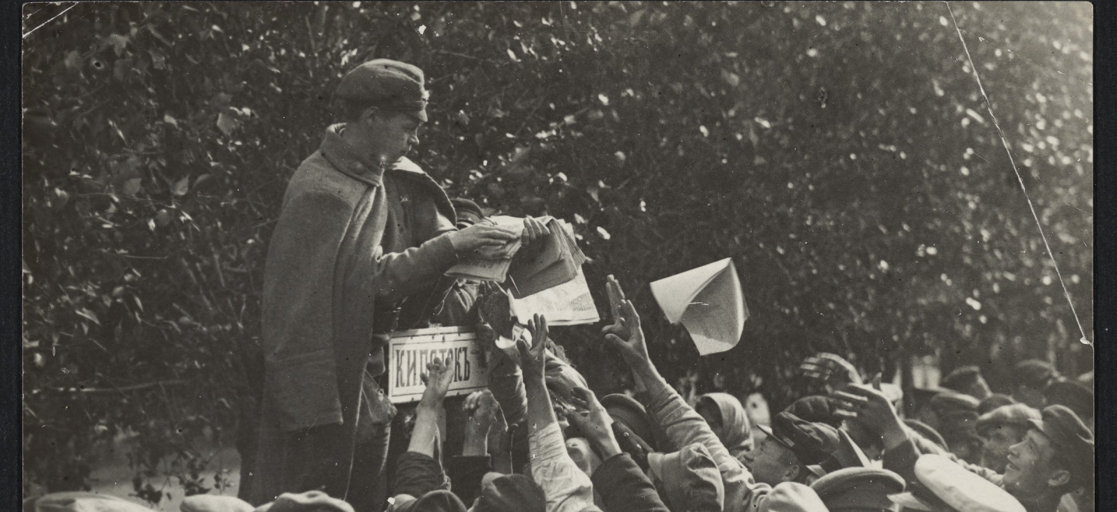 man standing above a crowd distributing newspapers