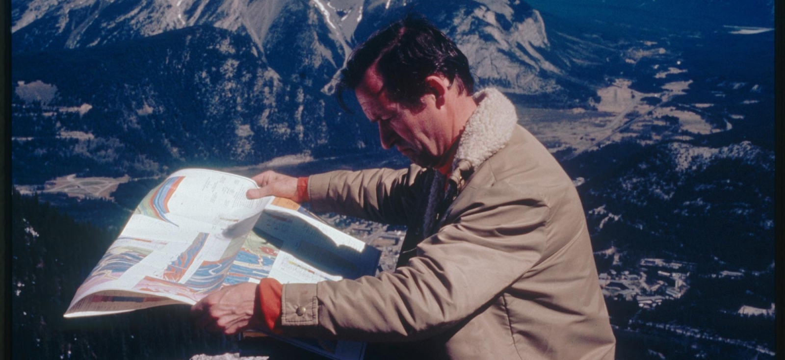 A picture of a man reading a map with mountains in the background. 