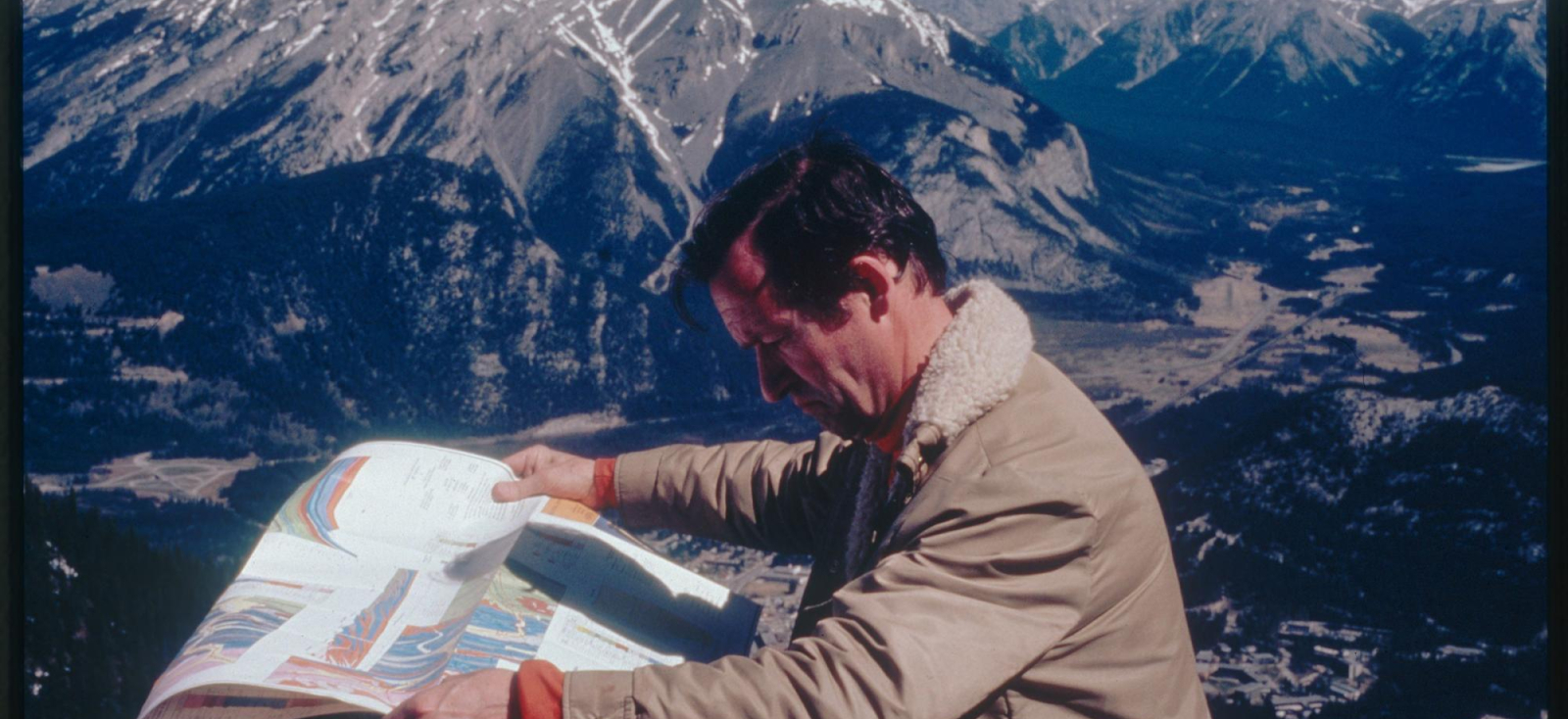 A picture of a man reading a map with mountains in the background. 