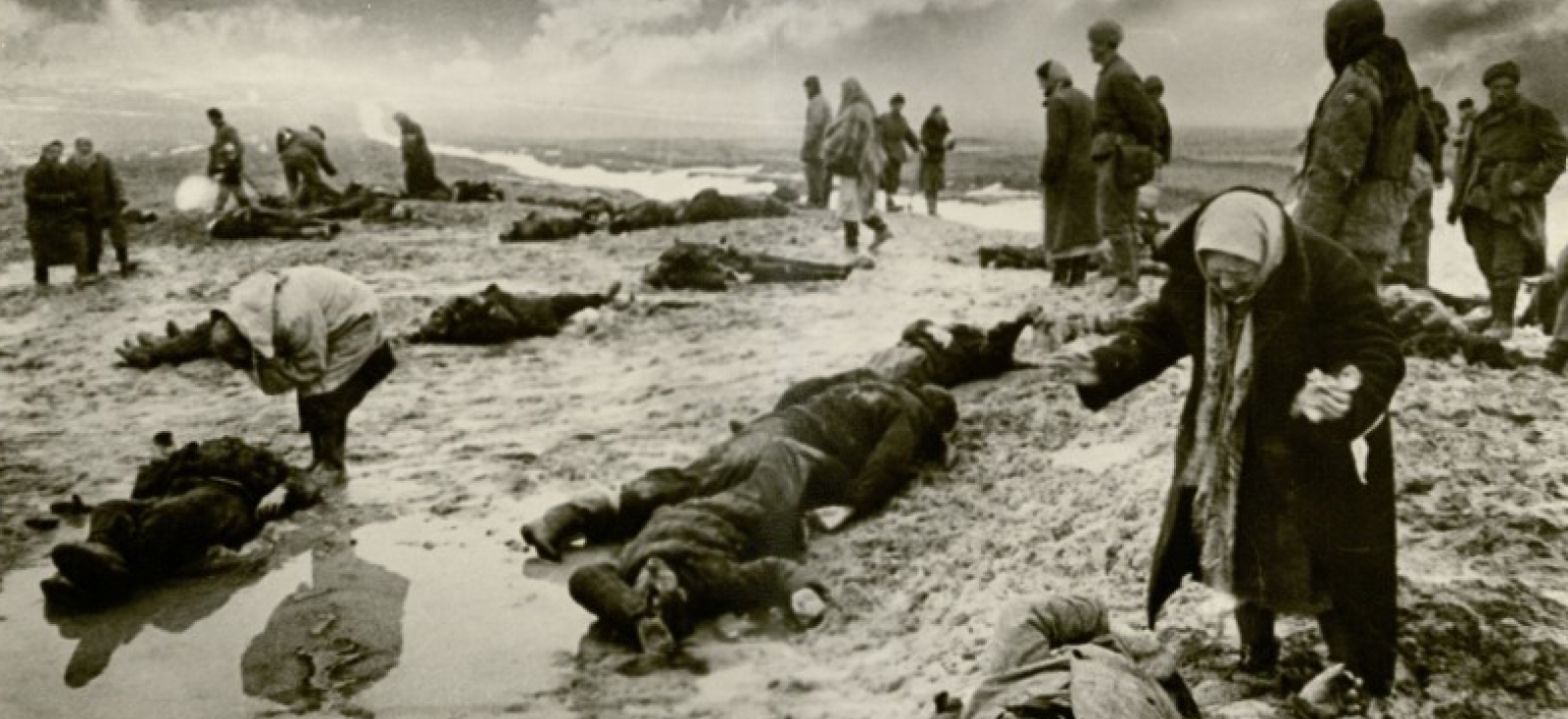 A group of people walking through a field littered with corpses