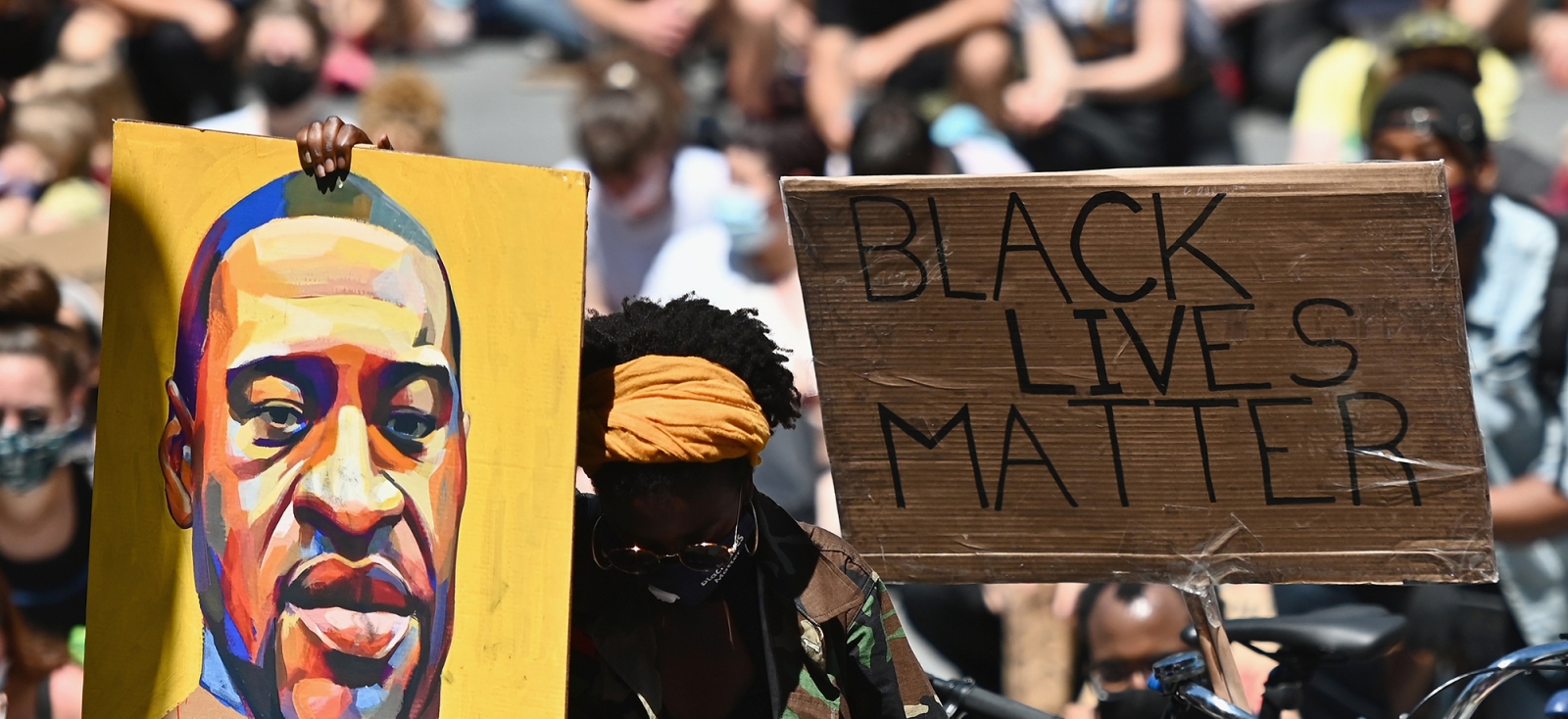 In a crowd of protesters, a painting of George Floyd next to a sign reading 'Black Lives Matter.'
