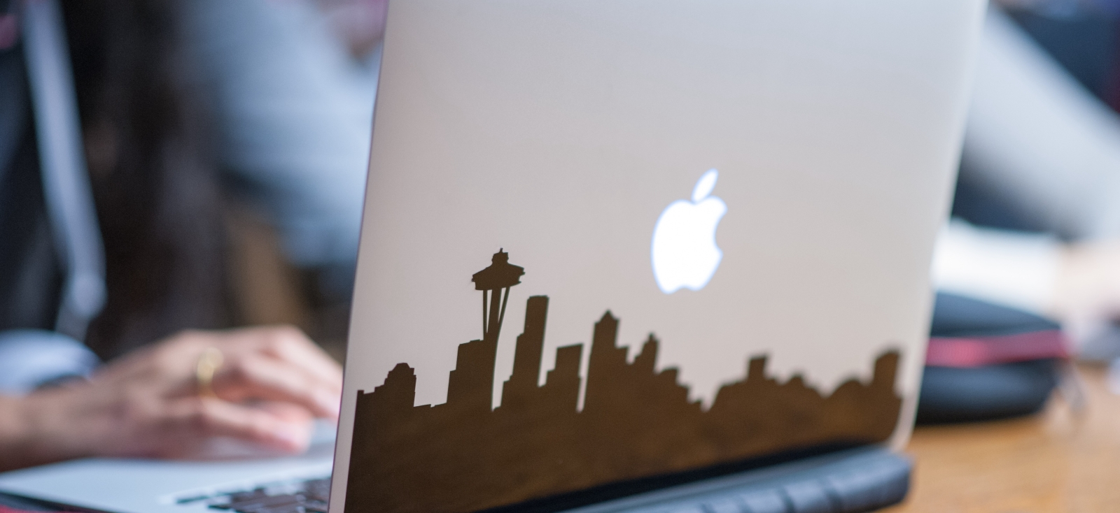 An open grey Macbook with a blurred hand at the keyboard