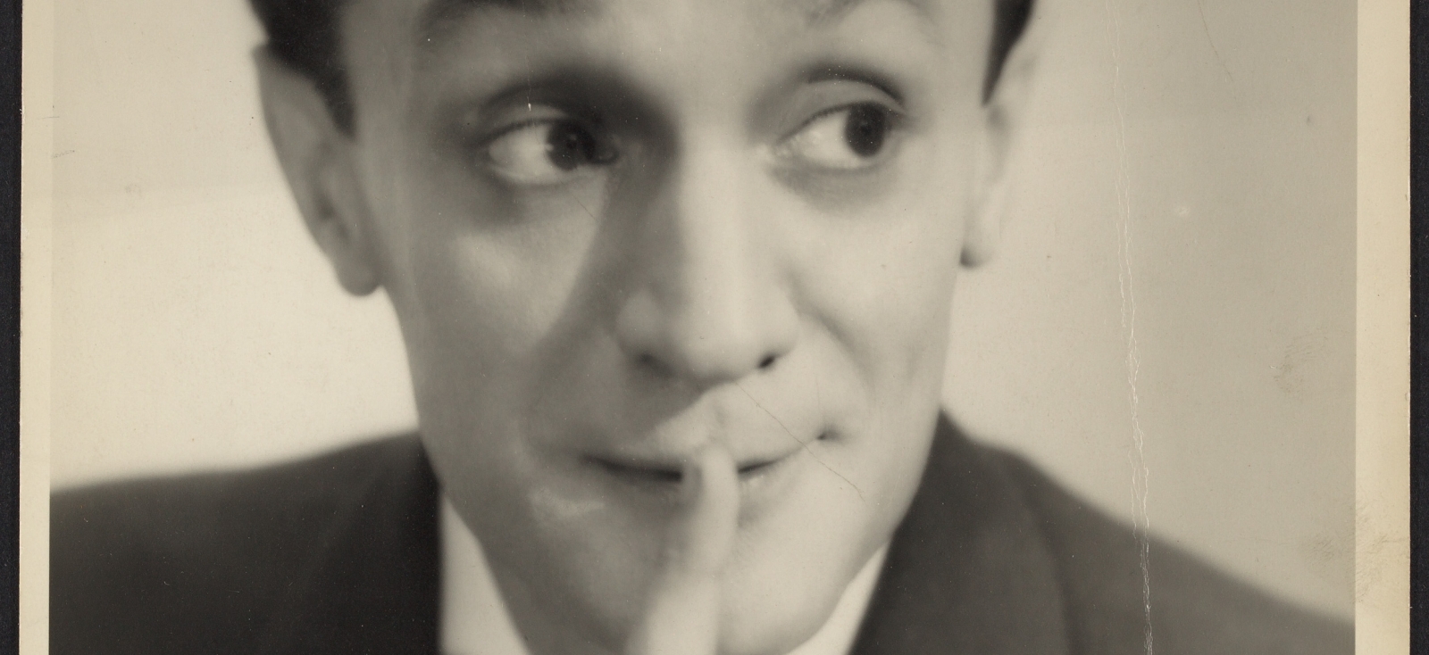 Leo Fuchs looks away from the camera and holds a finger up to his lips
