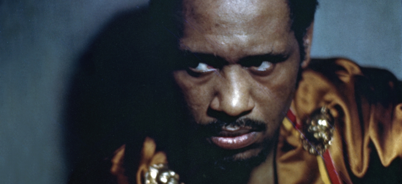 Paul Robeson as Othello, circa 1942. He has short black hair and is wearing a red top