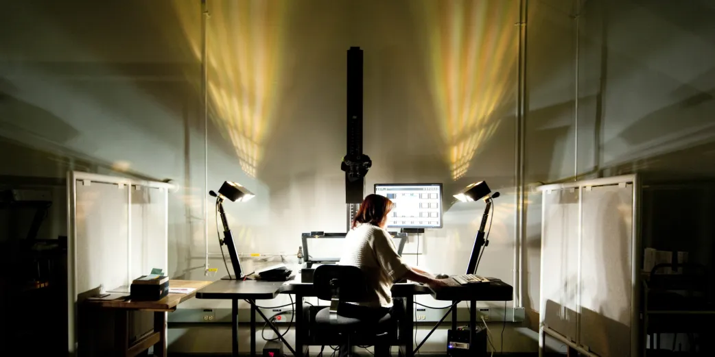 A library staff member sits in a dark studio scanning a rare book 