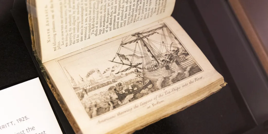 A photo of a book opened to a page featuring an illustration of "Americans throwing the cargoes of the tea ships into the river"