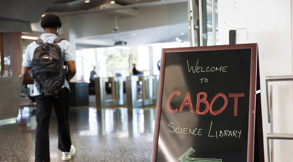 A man with a backpack walks past a sign that ways Welcome to Cabot Science Library