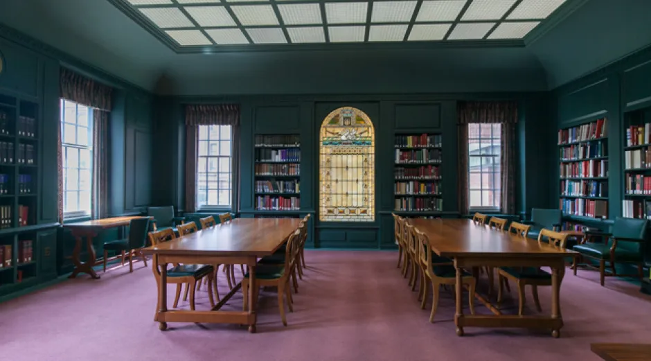 a reading room with green walls, wooden tables, and a stained glass window