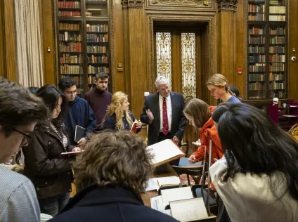 Peter Accardo talking to students in the Harry Widener Memorial Room. There's a display of books laid out on the table in front of them, which the students are checking out.