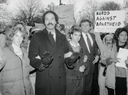 A black and white photo of Randall Robinson at a protest. Slogans say, "A.U. students for freedom in South Africa" and "Kurds against apartheid," and so on.