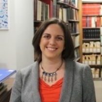 Photo of Amanda Hannoosh Steinberg in a gray blazer and red shirt, with bookshelves behind