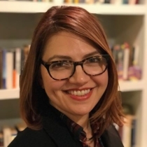 A headshot of Tamar standing in front of bookshelves. 