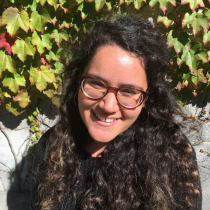 Headshot of smiling woman with glasses with a natural backdrop