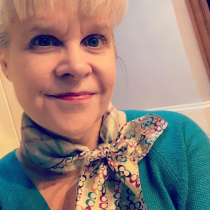 A picture of a blond white cisgender woman in a green sweater and a multi-colored scarf.
