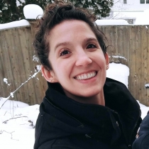 Smiling woman standing in the snow. She is fair skinned with dark hair.
