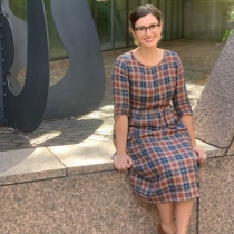 Image of a woman seated outside a library with abstract sculpture.