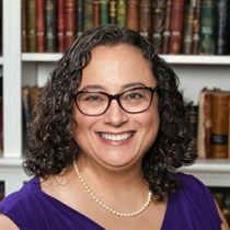Picture of a white woman with curly brown hair and glasses in front of a book shelf