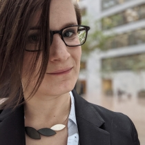 Photo of Claire in the Hart Senate office building. Wearing a suit jacket, resin necklace, glasses