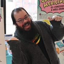 Matthew emoting excitedly in front of the Graphic Medicine Exhibit displayed at Countway Library in 2024